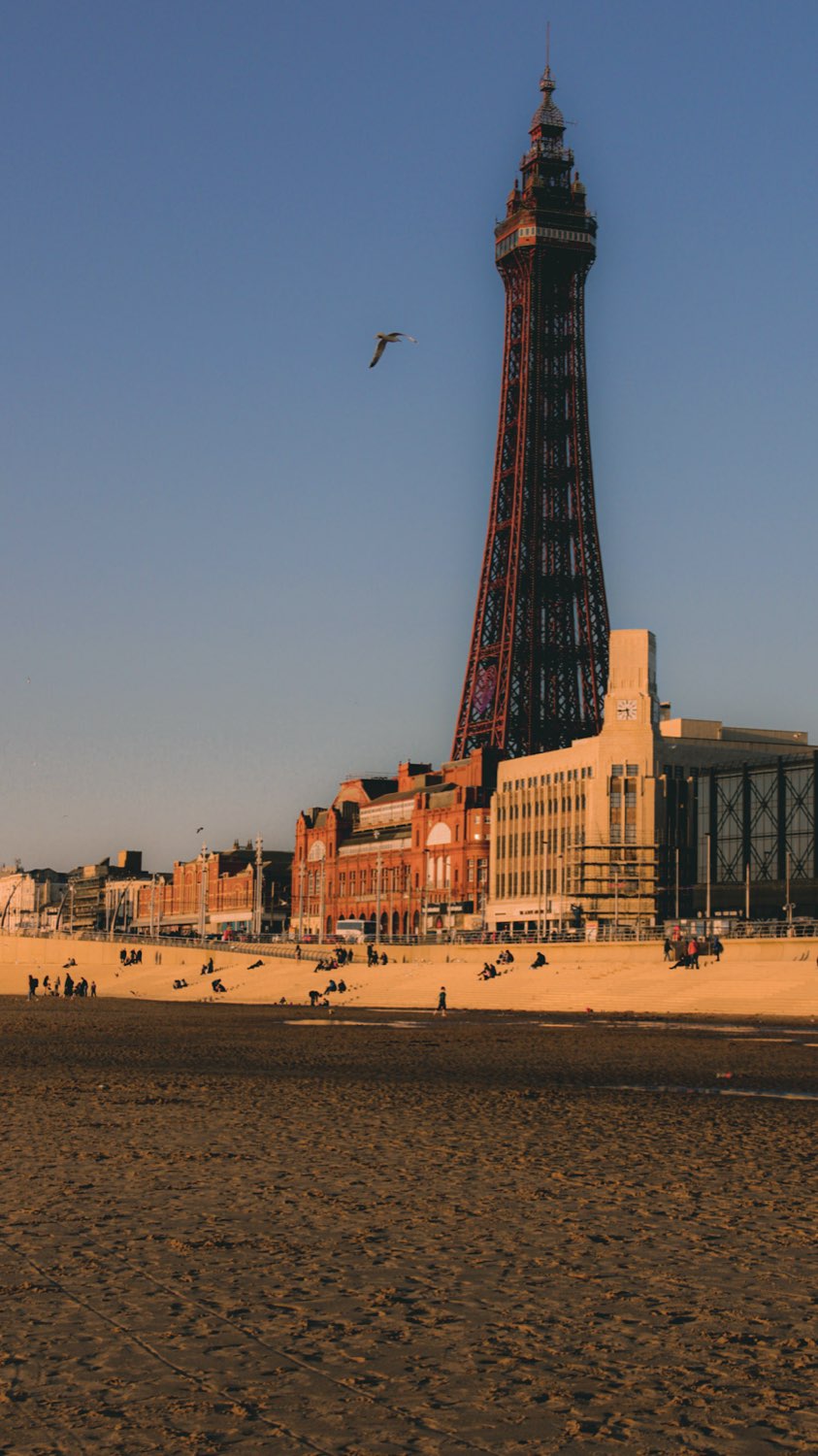 Blackpool Tower and the seafront in low golden light, seen across a wide empty beach