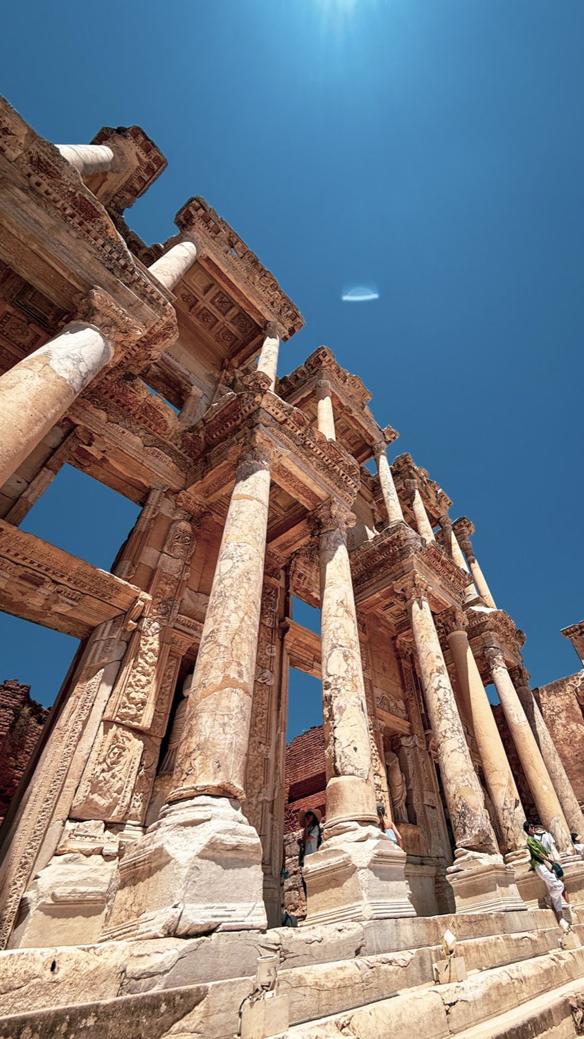 The columned marble façade of the Library of Celsus seen from below against a deep blue sky