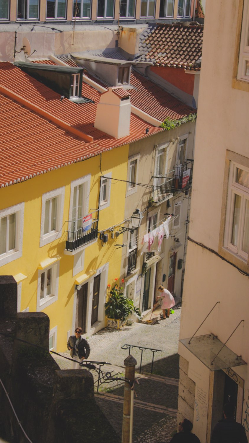 A narrow Lisbon street of yellow and white buildings with washing hung out and a stairway below