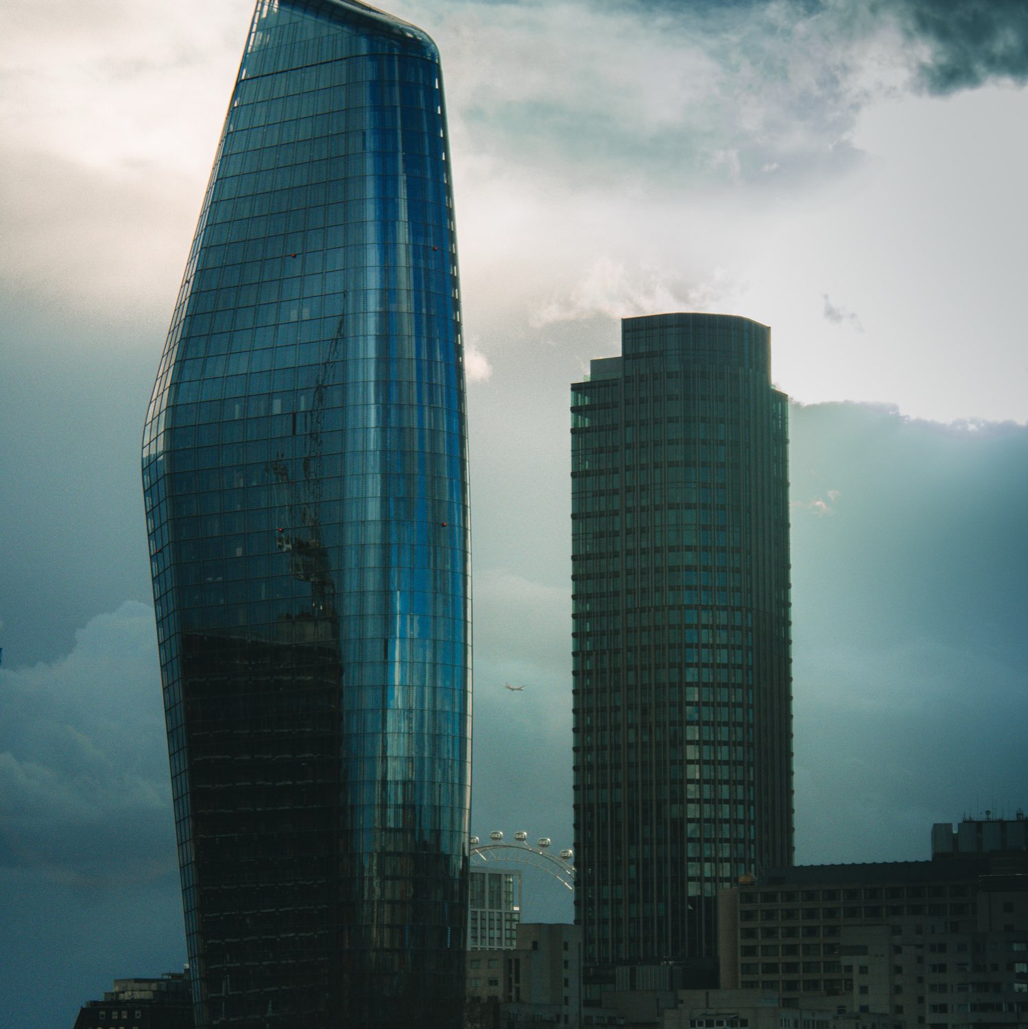 A curved blue glass tower and a rectangular office block against a heavy grey sky