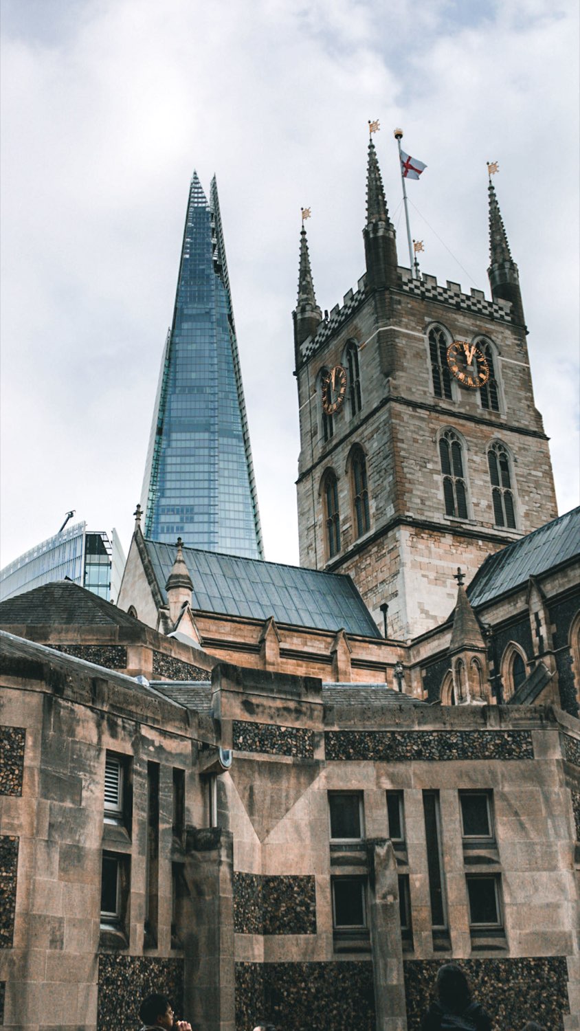The stone clock tower of Southwark Cathedral in front of the tapering glass Shard