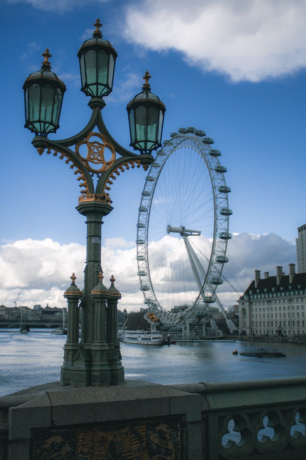An ornate green and gold lamp post on Westminster Bridge with the London Eye behind it